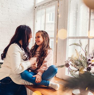 Parent and child sitting next to a window smiling at one another.