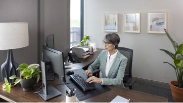 Woman sitting behind a desk in an office typing on a computer keyboard.