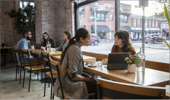 Two women at a coffee shop talking and looking at a tablet