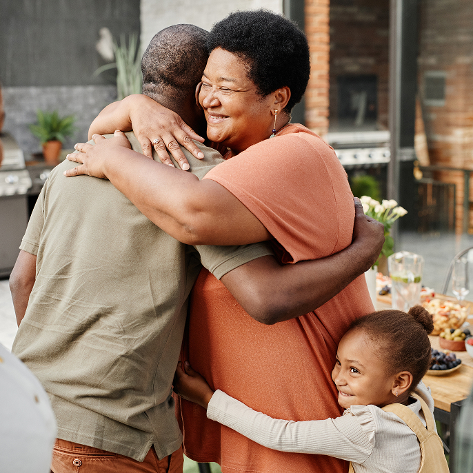 Man and woman hugging and a young girl is hugging the woman’s waist and smiling