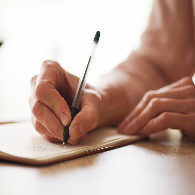 Close up of a hand holding a pen and writing in a notebook.
